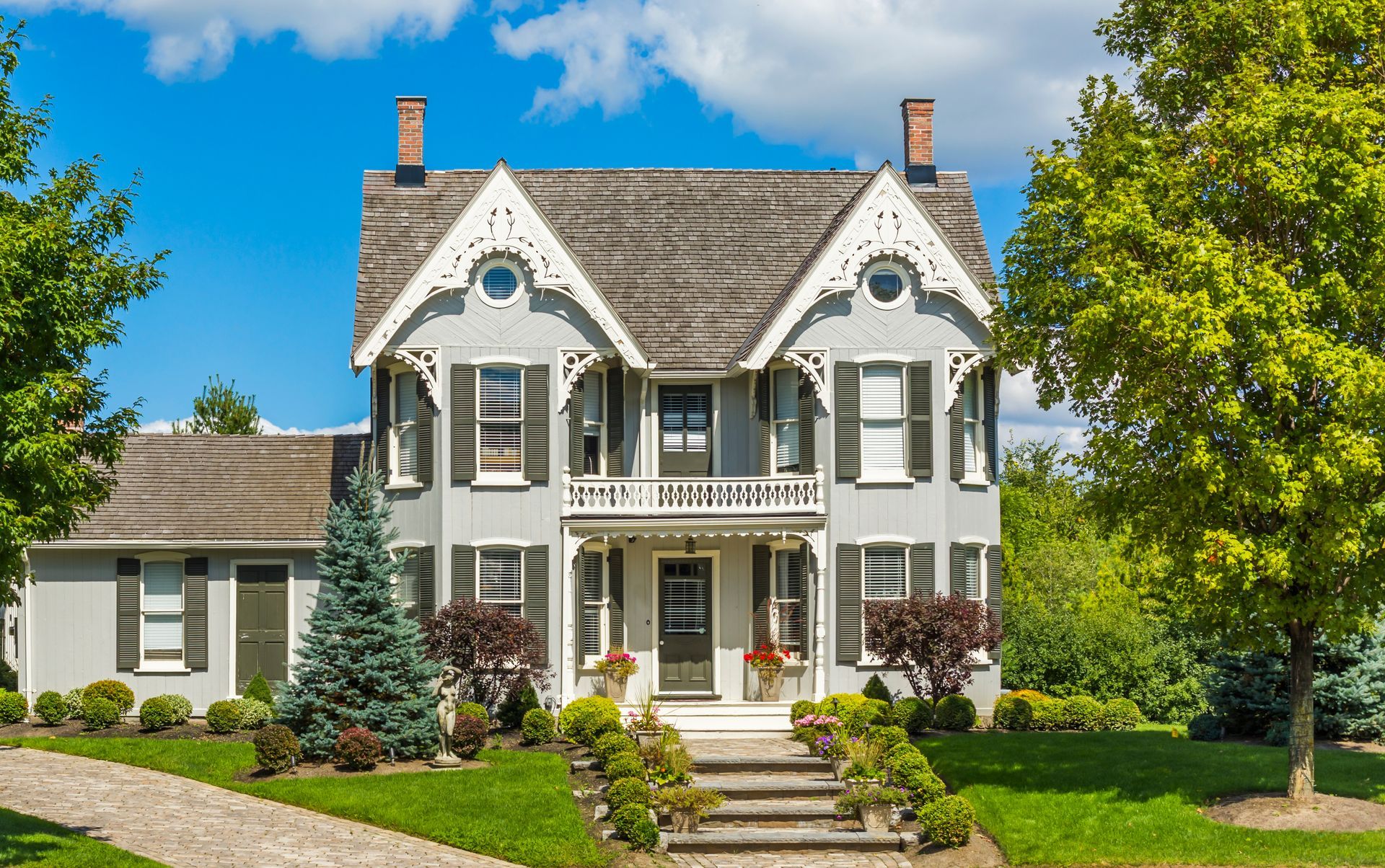 A large white house with a gray roof and white shutters is sitting on top of a lush green lawn.