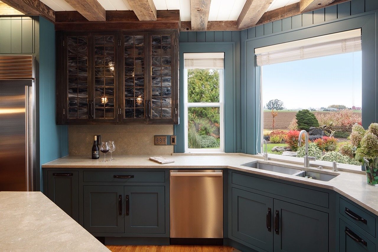 Kitchen with blue cabinets, stainless steel appliances, and a large window overlooking a garden.
