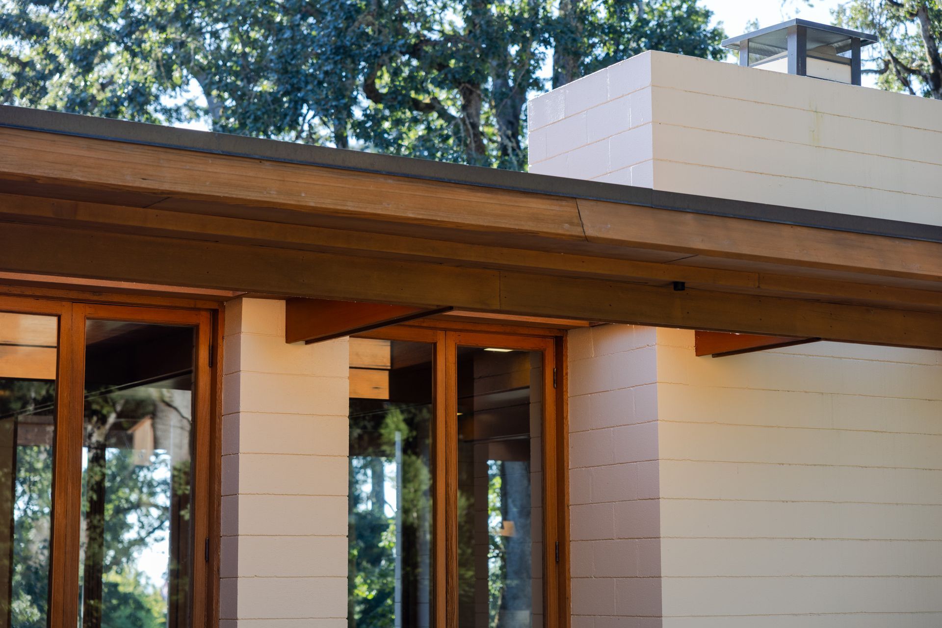 Close-up view of a building's exterior with wooden beams, large windows, and a light-colored wall.