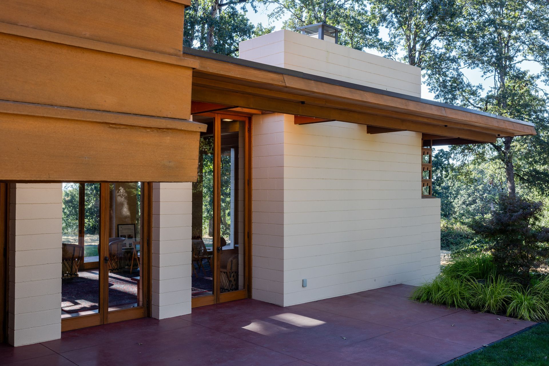 Exterior of a light brick building with wooden accents, glass doors, and a red concrete patio.