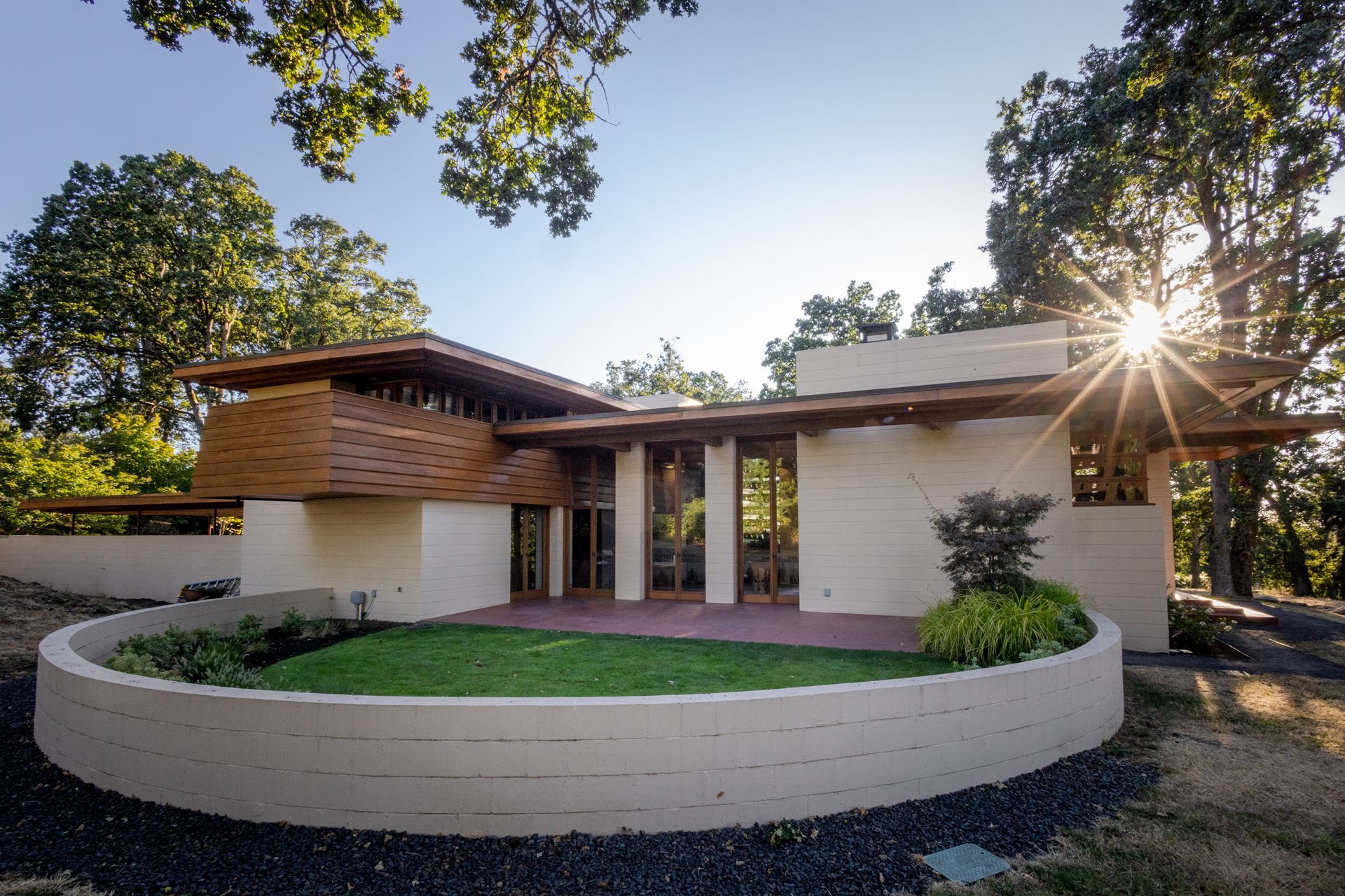 Modern home with low, flat roof, and curved wall in front, with sun shining through trees.