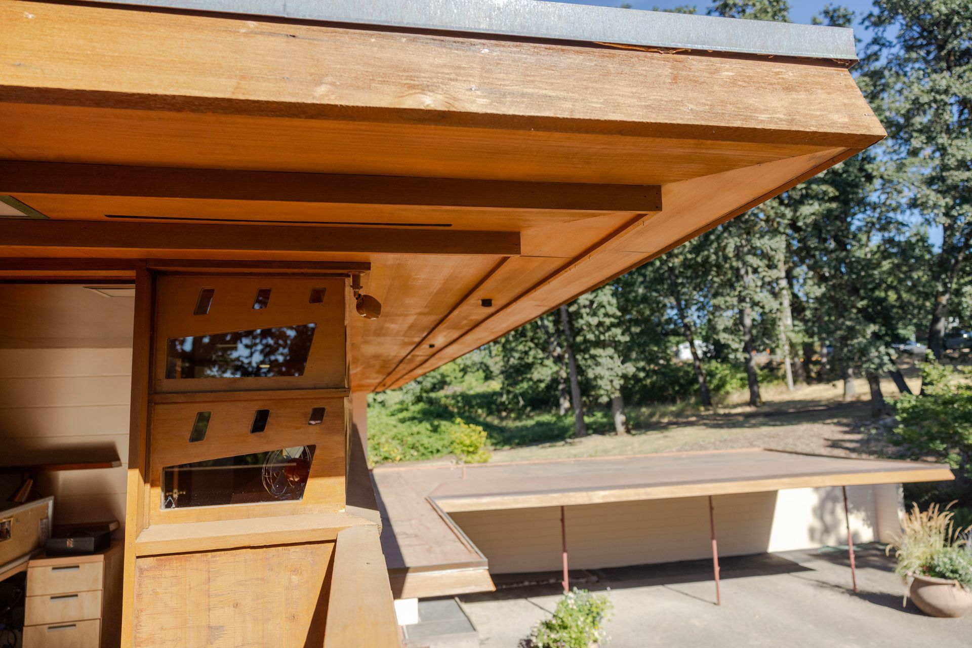 Wooden house with an overhanging roof, a window with angled cutouts, and a carport.