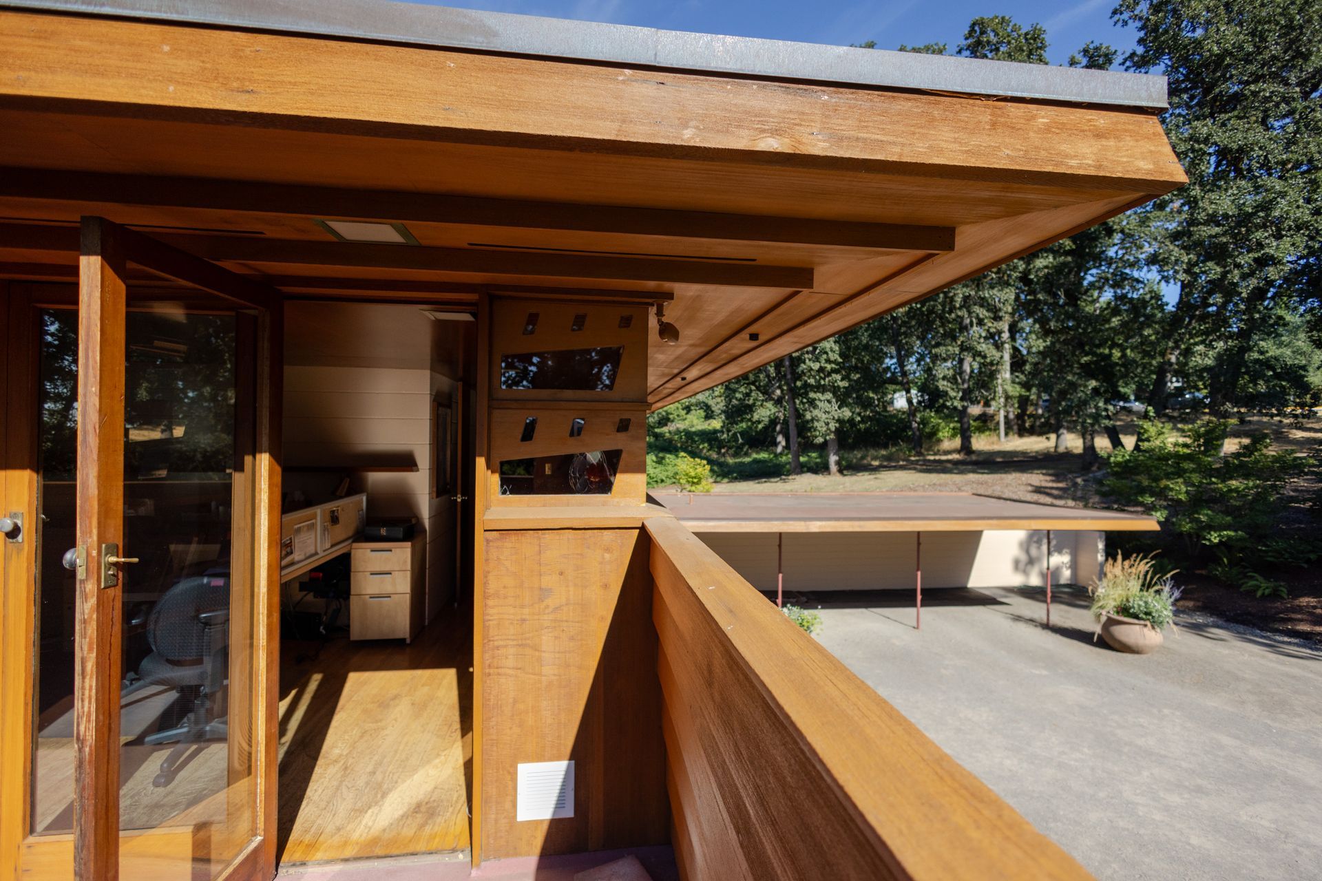 Exterior of a wooden structure with a long overhang, balcony, and open glass doors.