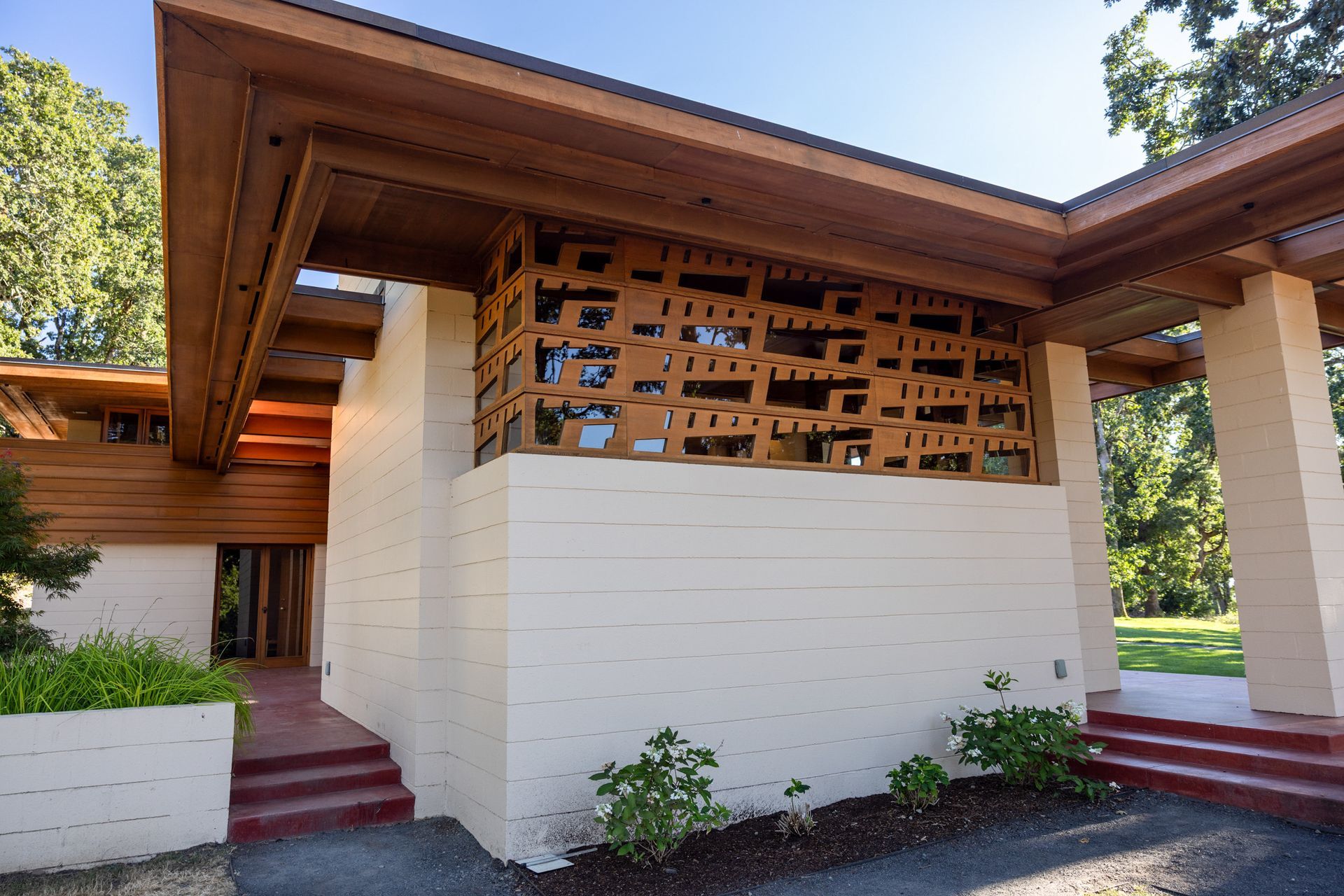 Beige and wood building exterior with geometric openings and a red entryway.