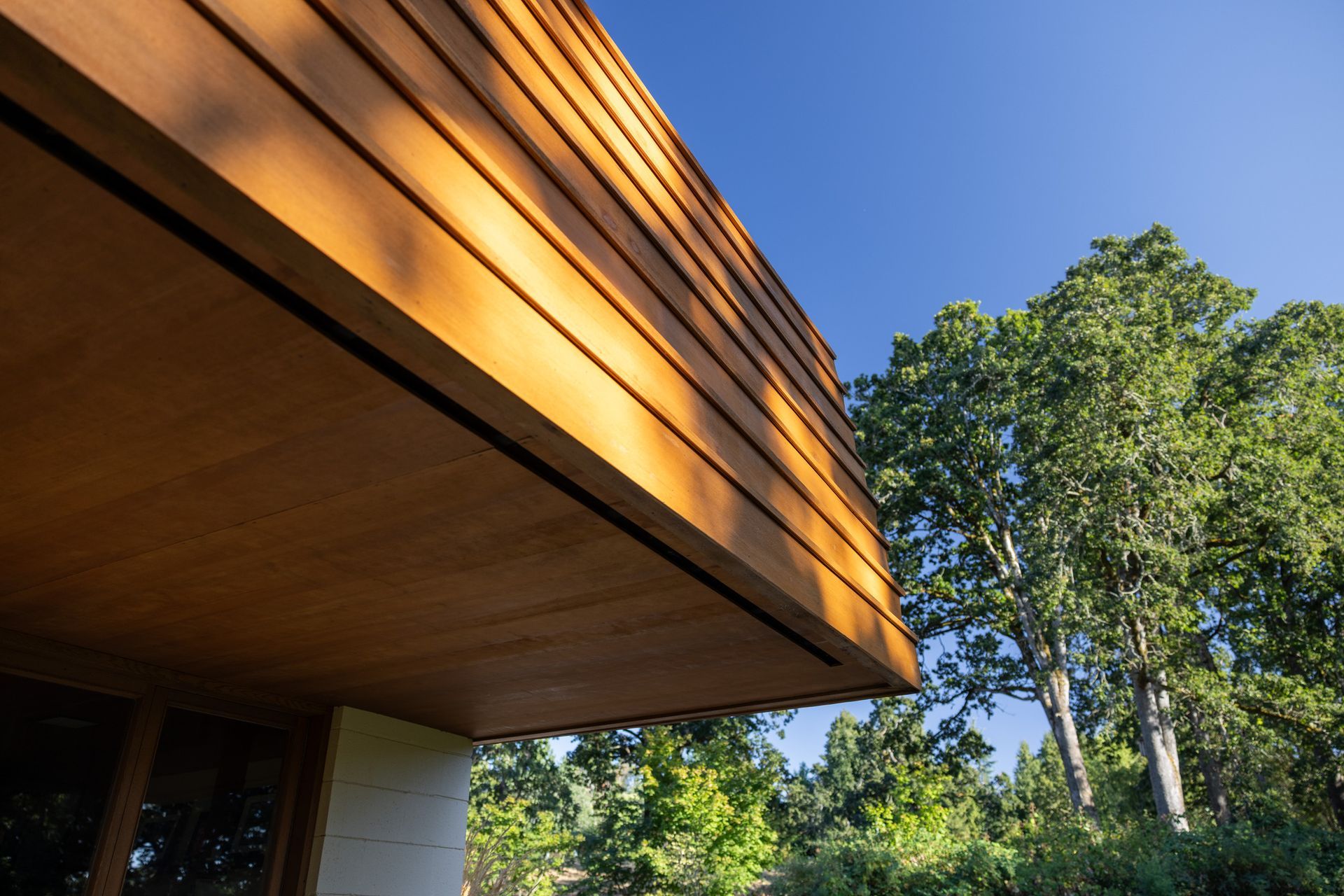 Wooden building exterior with dark trim and trees against a bright blue sky.