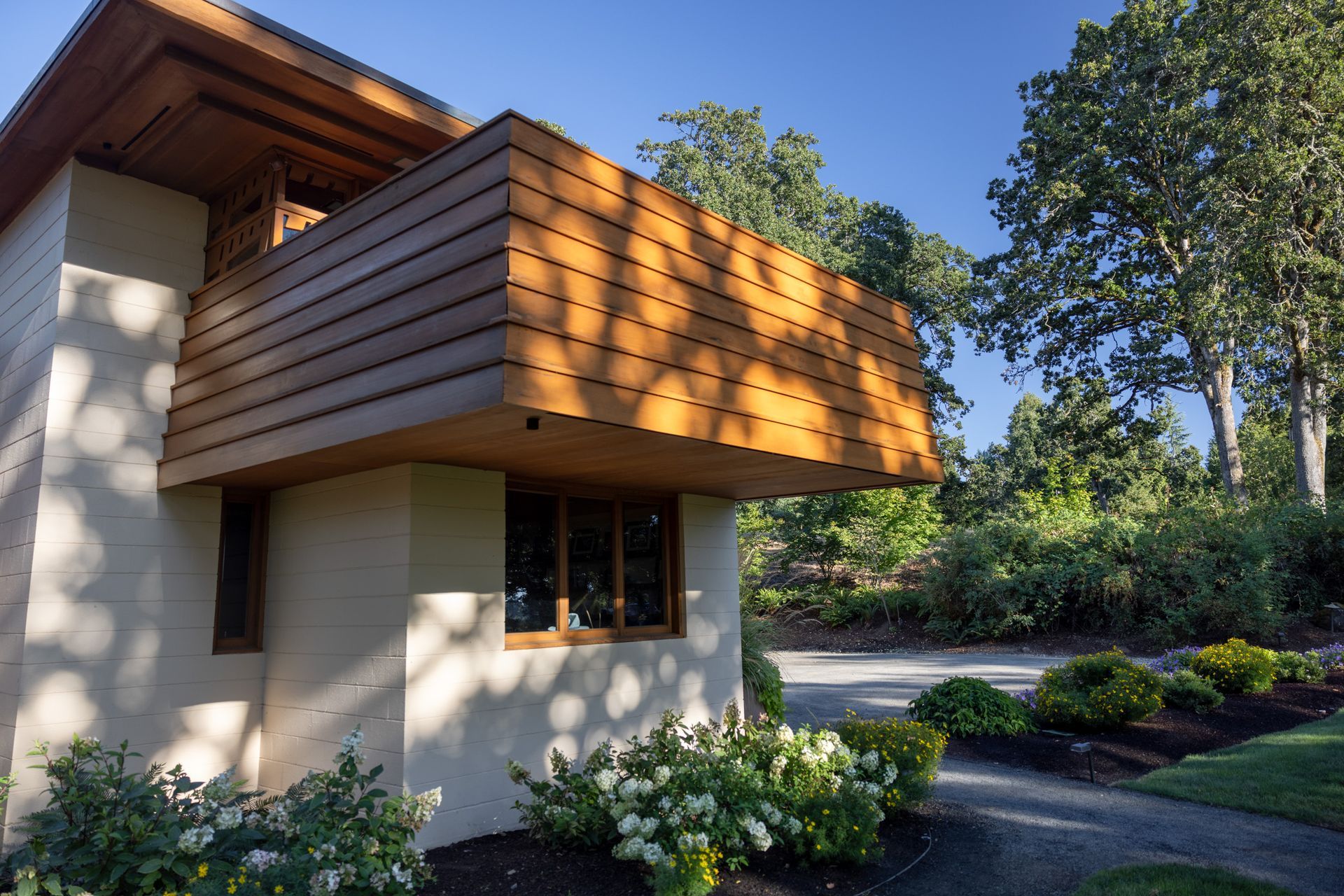 Modern house with brown wooden overhang, windows, and manicured landscaping under a bright sky.