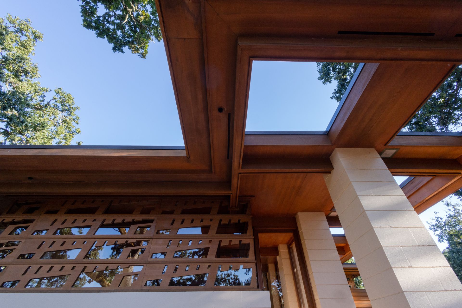 Wooden architectural detail with geometric openings, and stone columns against a blue sky.