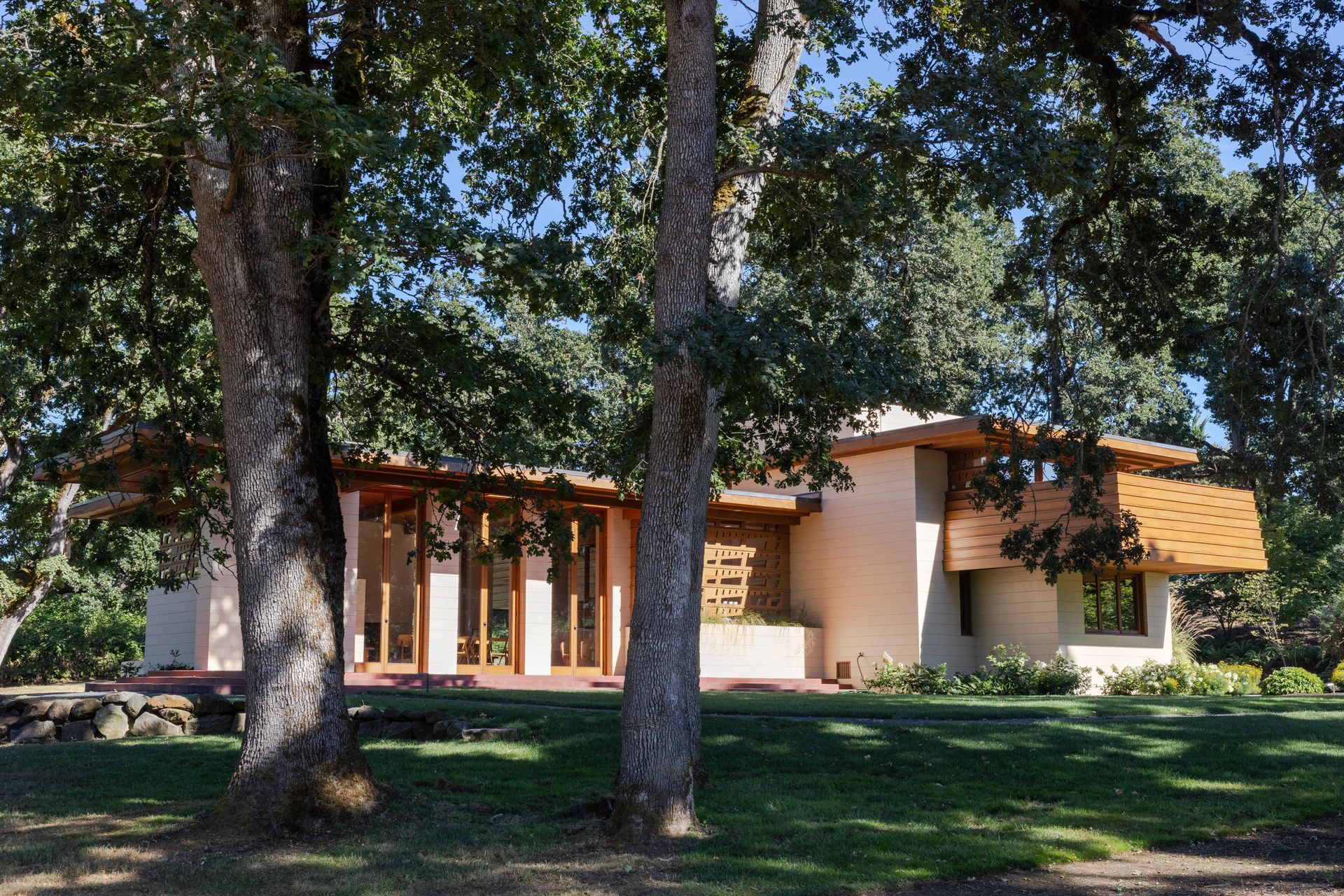 Modern home with tan stucco walls and wooden accents framed by trees on a sunny day.