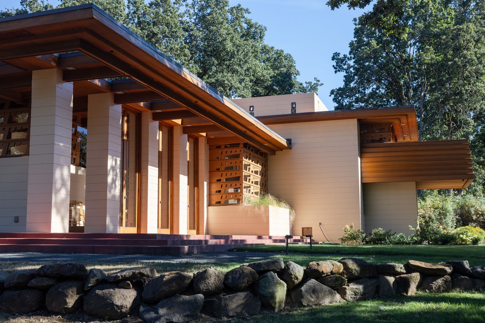Beige and wood Craftsman-style house with pillars, long eaves, and a stone retaining wall.