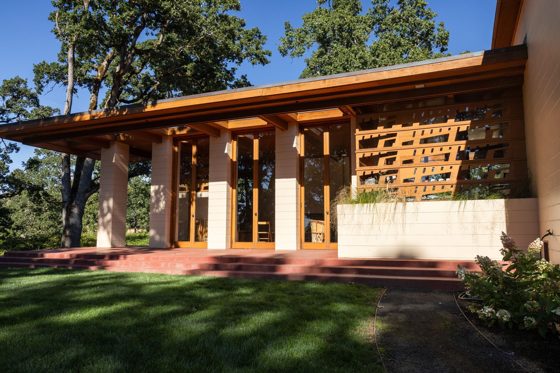 A low-slung, reddish-brown and beige house with a covered entryway and a red-tiled patio, on a grassy lawn.