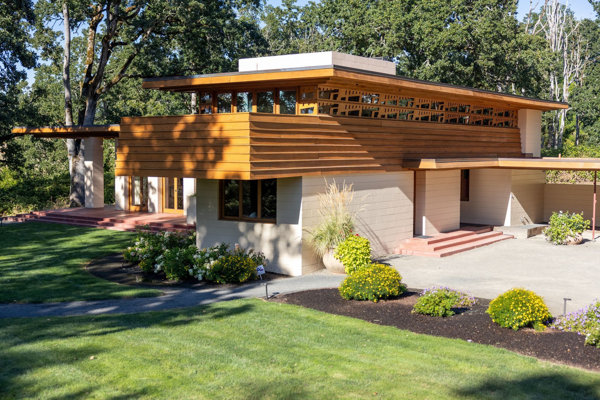 Mid-century modern home with wood trim, low-pitched roof, and cantilevered sections. Lawn and garden in front.