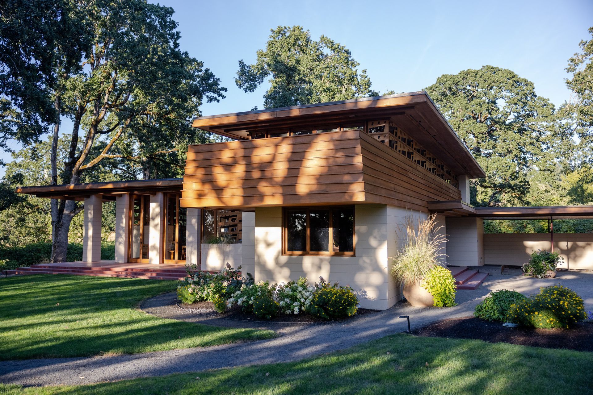 Mid-century modern home with wood accents and a covered porch, set on a grassy lawn with trees.