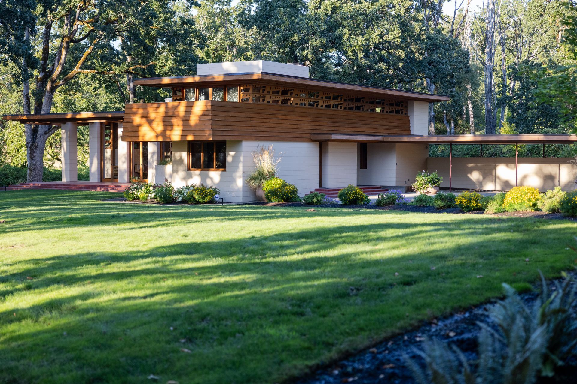 Modern house with wooden accents and a flat roof, set in a green yard with trees.