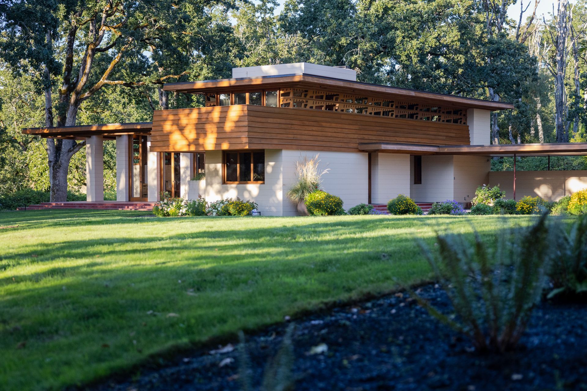 Low-angle view of a light-colored prairie-style house with wooden accents; set on a manicured green lawn.