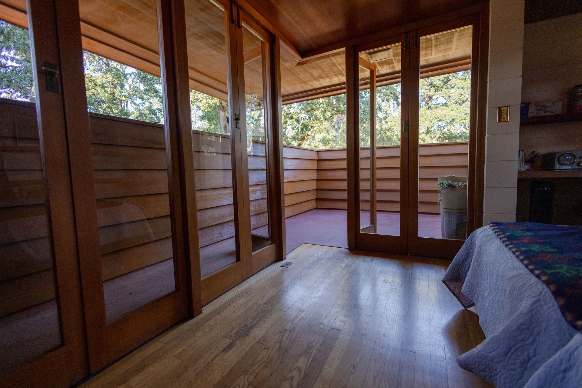Bedroom with wood flooring and sliding glass doors leading to a balcony with horizontal wooden railings.