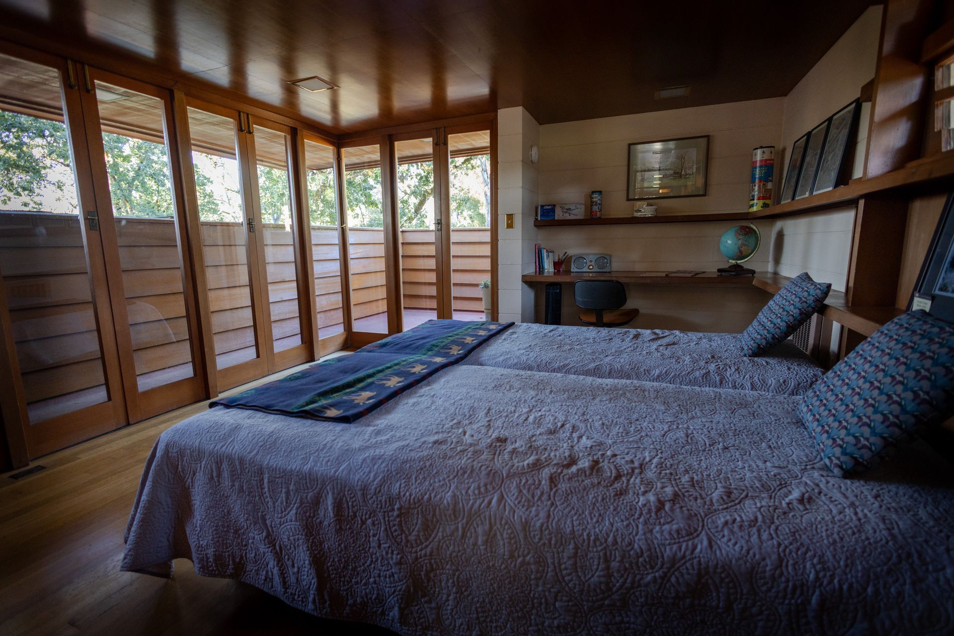 Bedroom with two twin beds, wooden walls and doors, overlooking greenery.