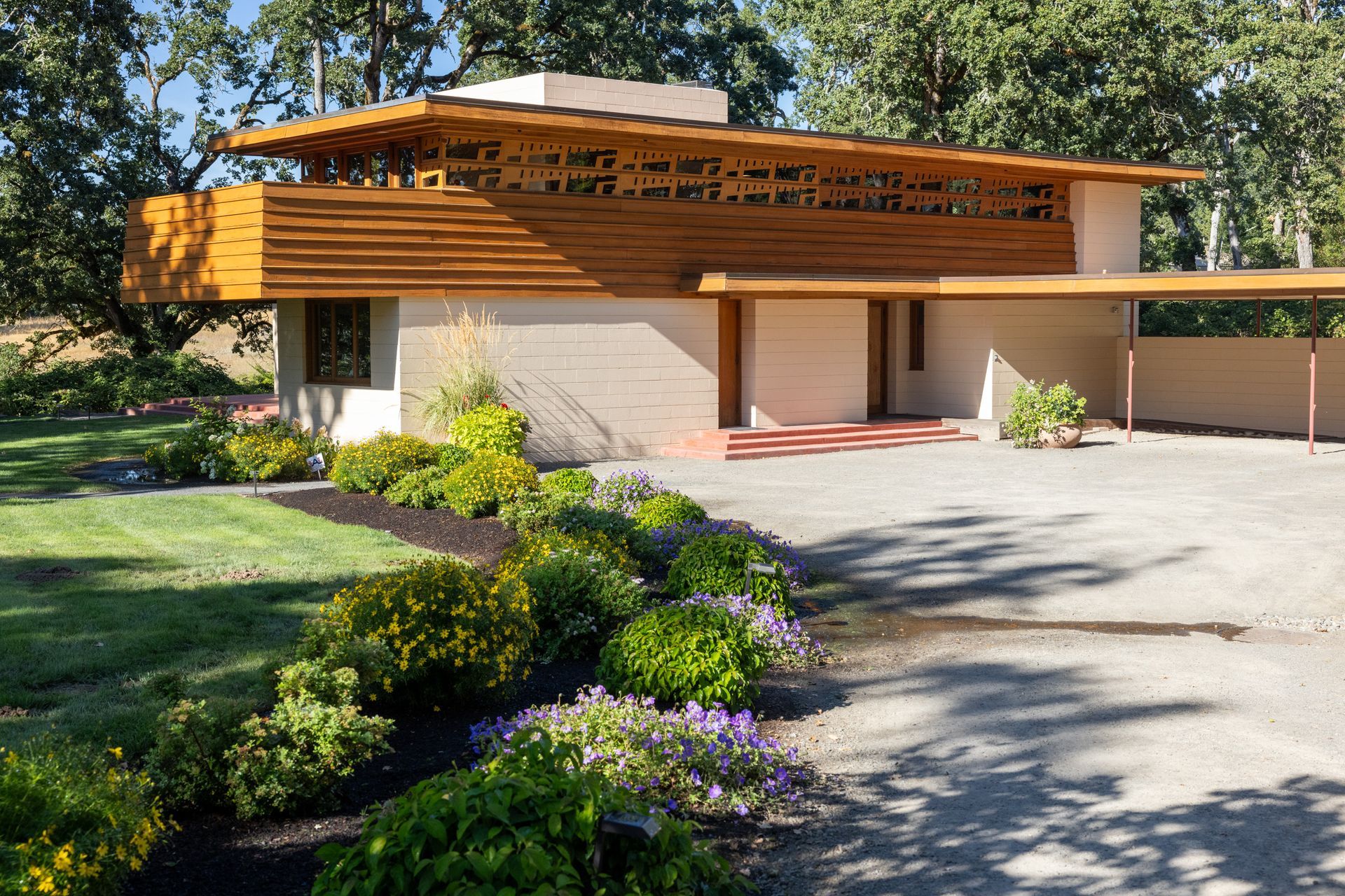 Mid-century modern home with wood accents, a flat roof, and a gravel driveway in a lush green setting.