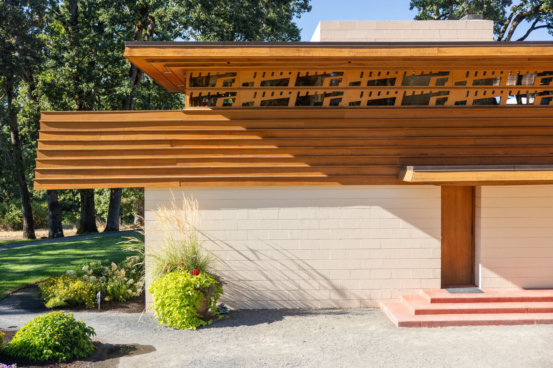 Beige brick building with wood trim and accents, featuring a sloped roof, front entrance, and landscaping.