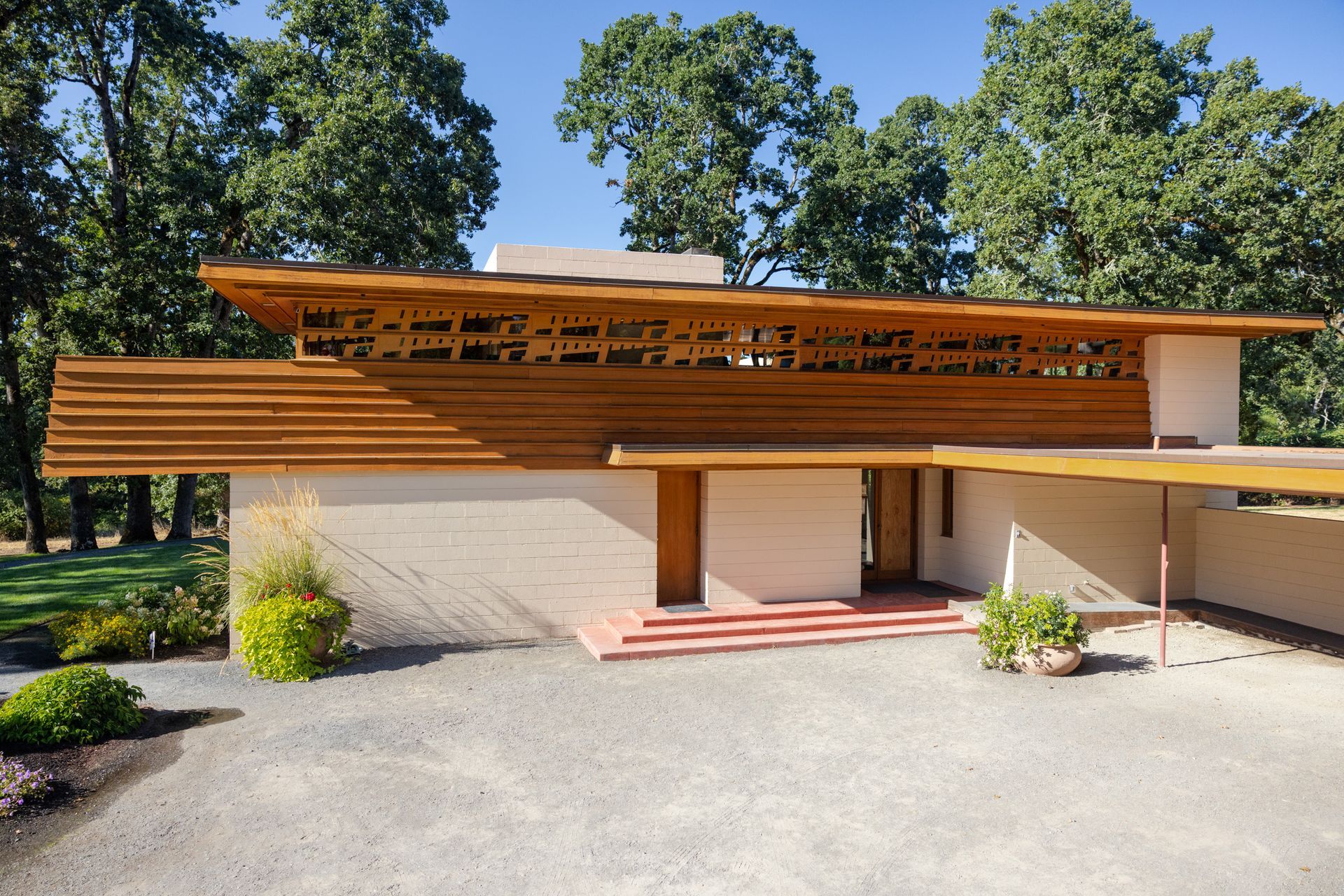 Mid-century modern home with horizontal wood siding and decorative patterned beams, on a gravel driveway.