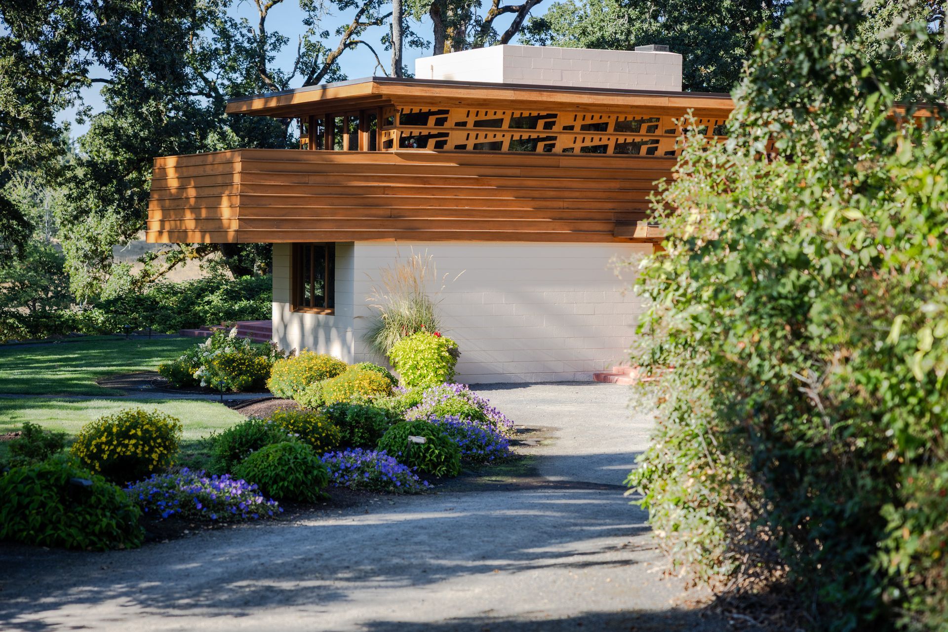 A small, white building with a wooden overhang surrounded by bushes and a pathway.