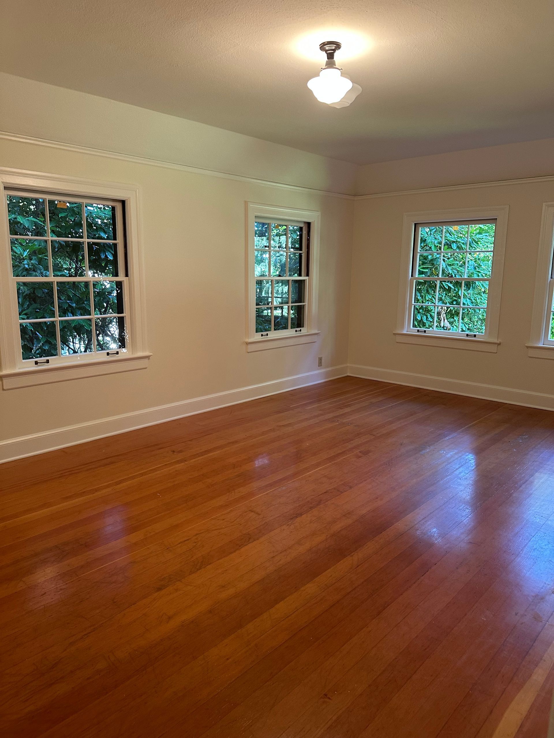 An empty room with hardwood floors and three windows.