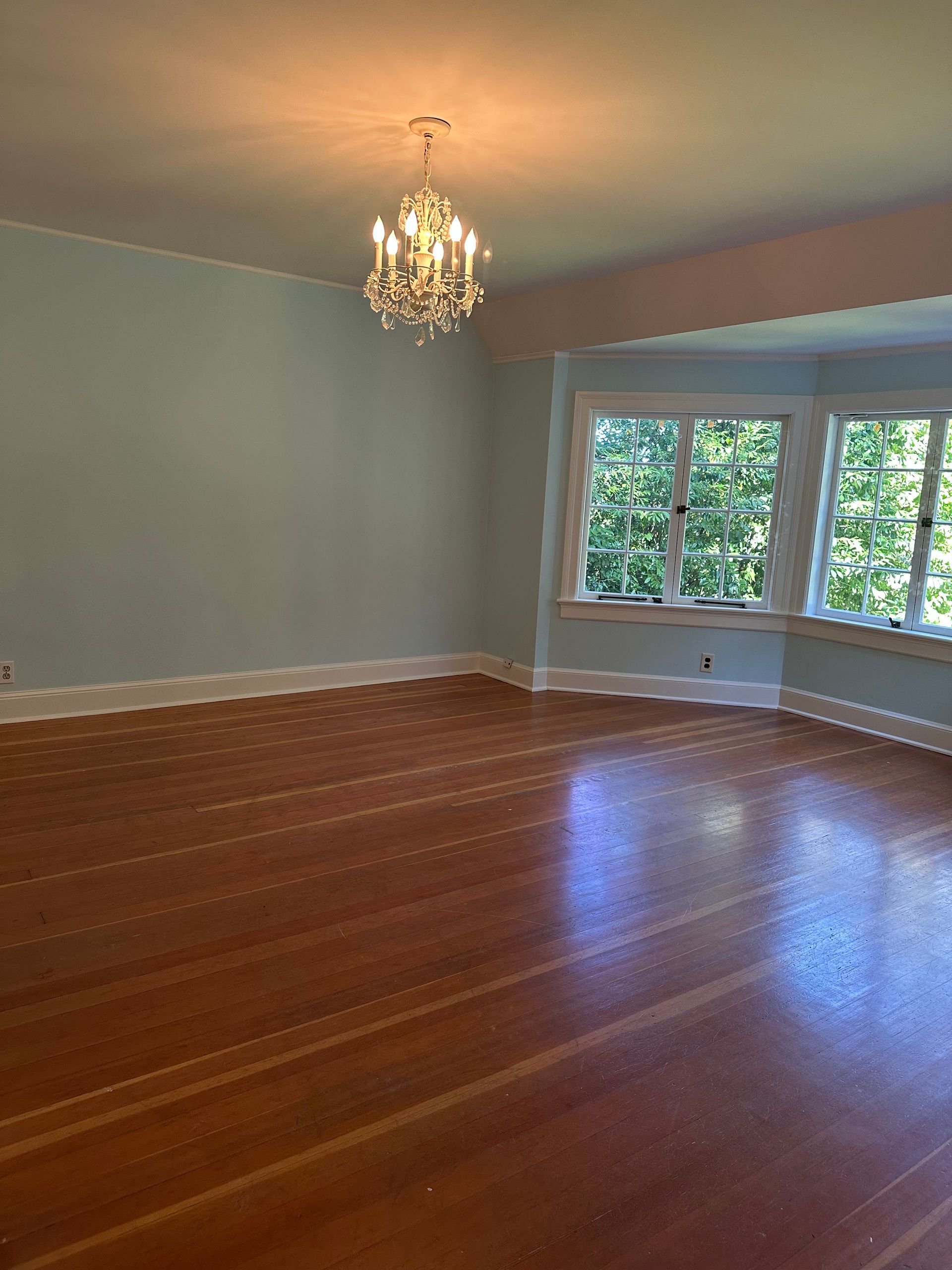 An empty living room with hardwood floors and a chandelier.