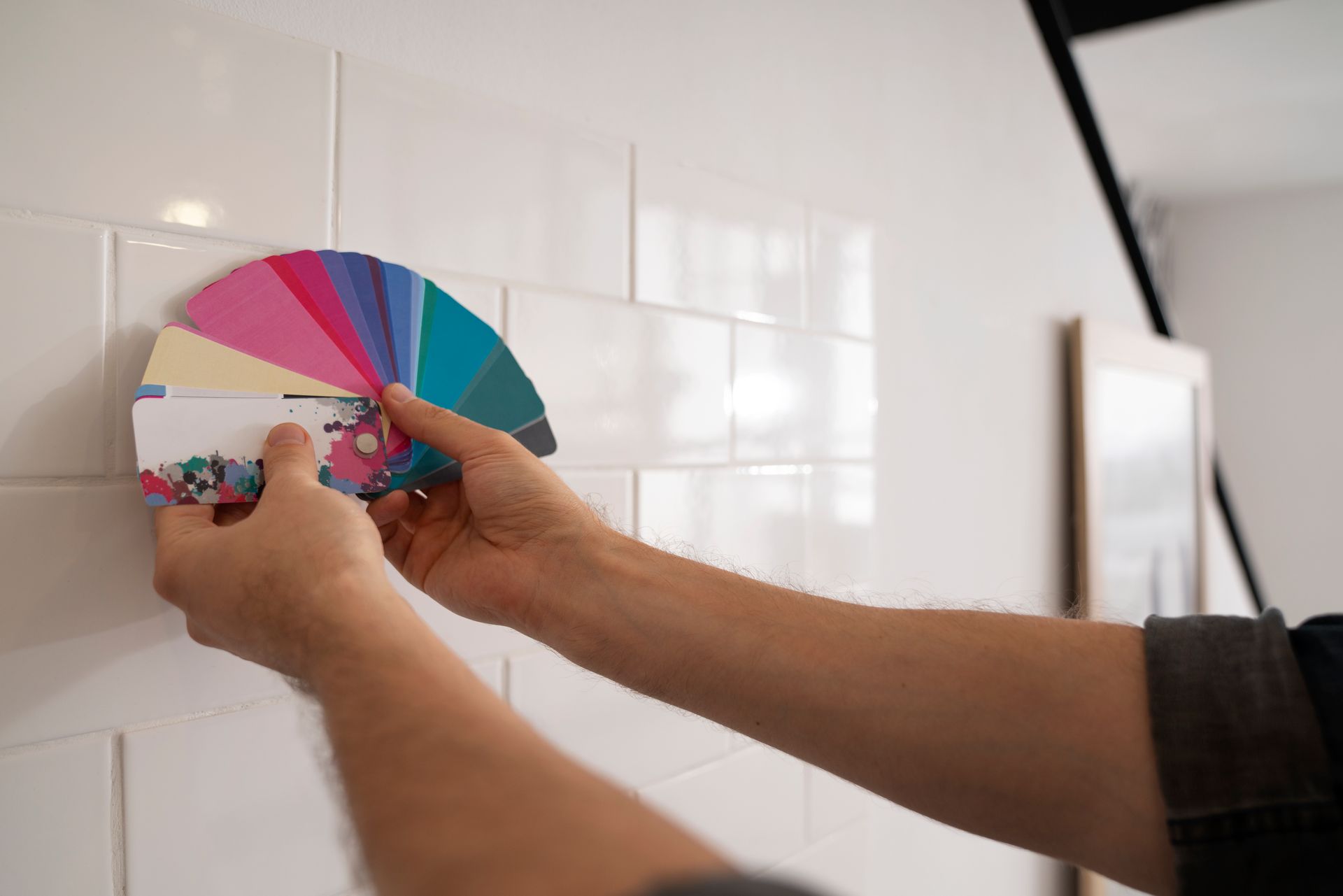 Person holding a color palette against white tiles, choosing paint colors.