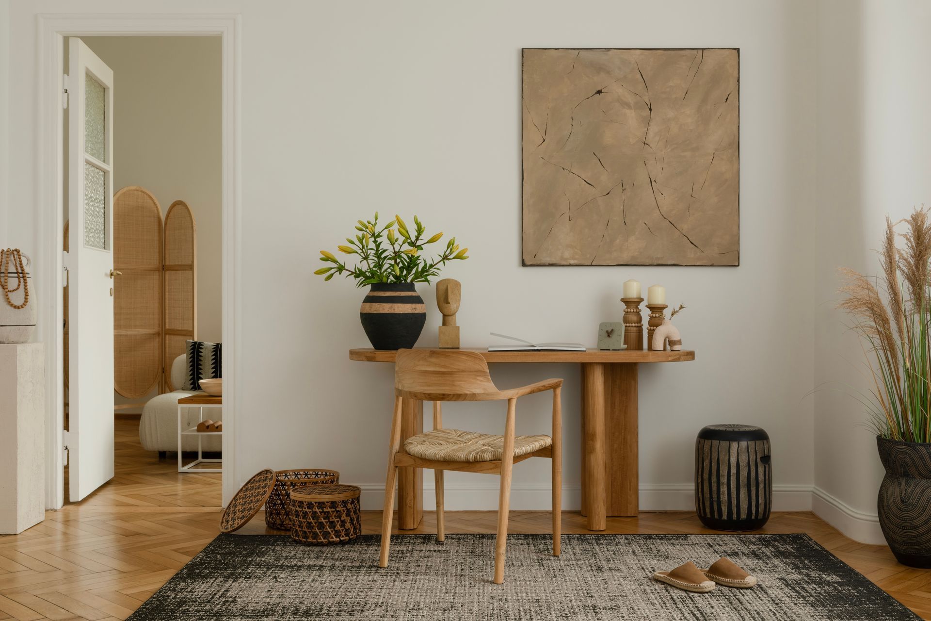 Minimalist home office with wooden desk, chair, potted plant, woven rug, and neutral decor