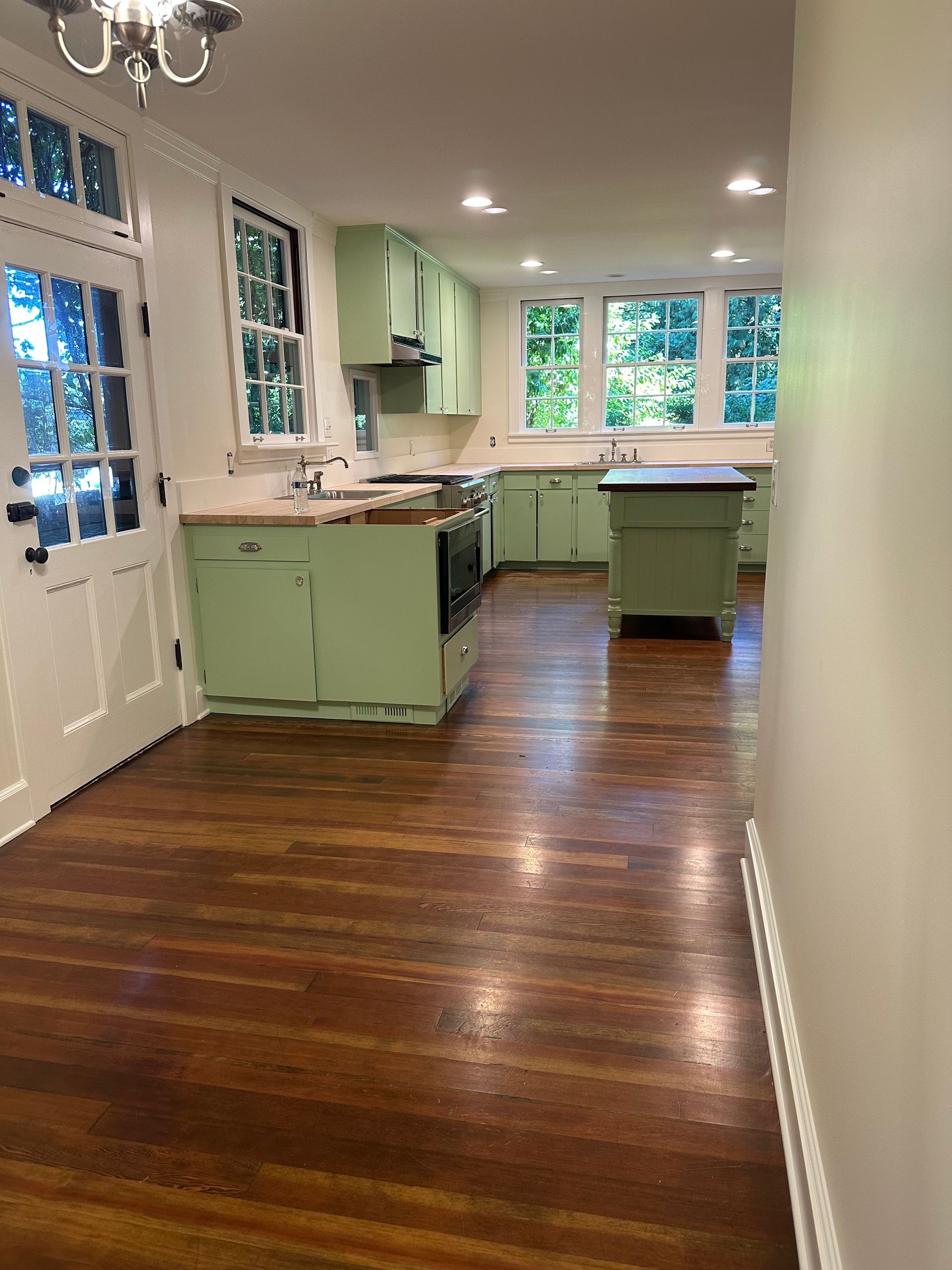 An empty kitchen with green cabinets and wooden floors.