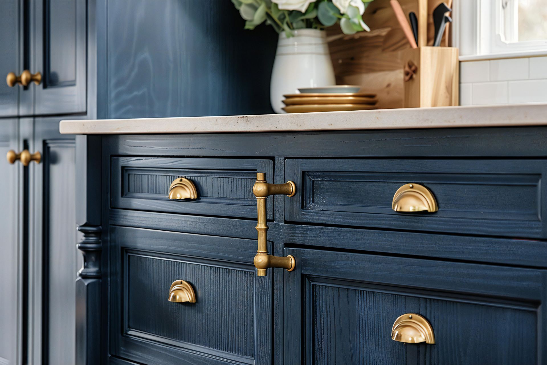 Navy blue kitchen cabinet with brass pulls beneath a white countertop and decor above