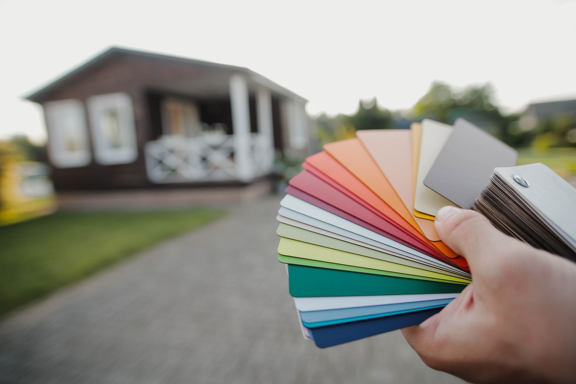 Hand holding a fan of colorful paint swatches in front of a house under renovation