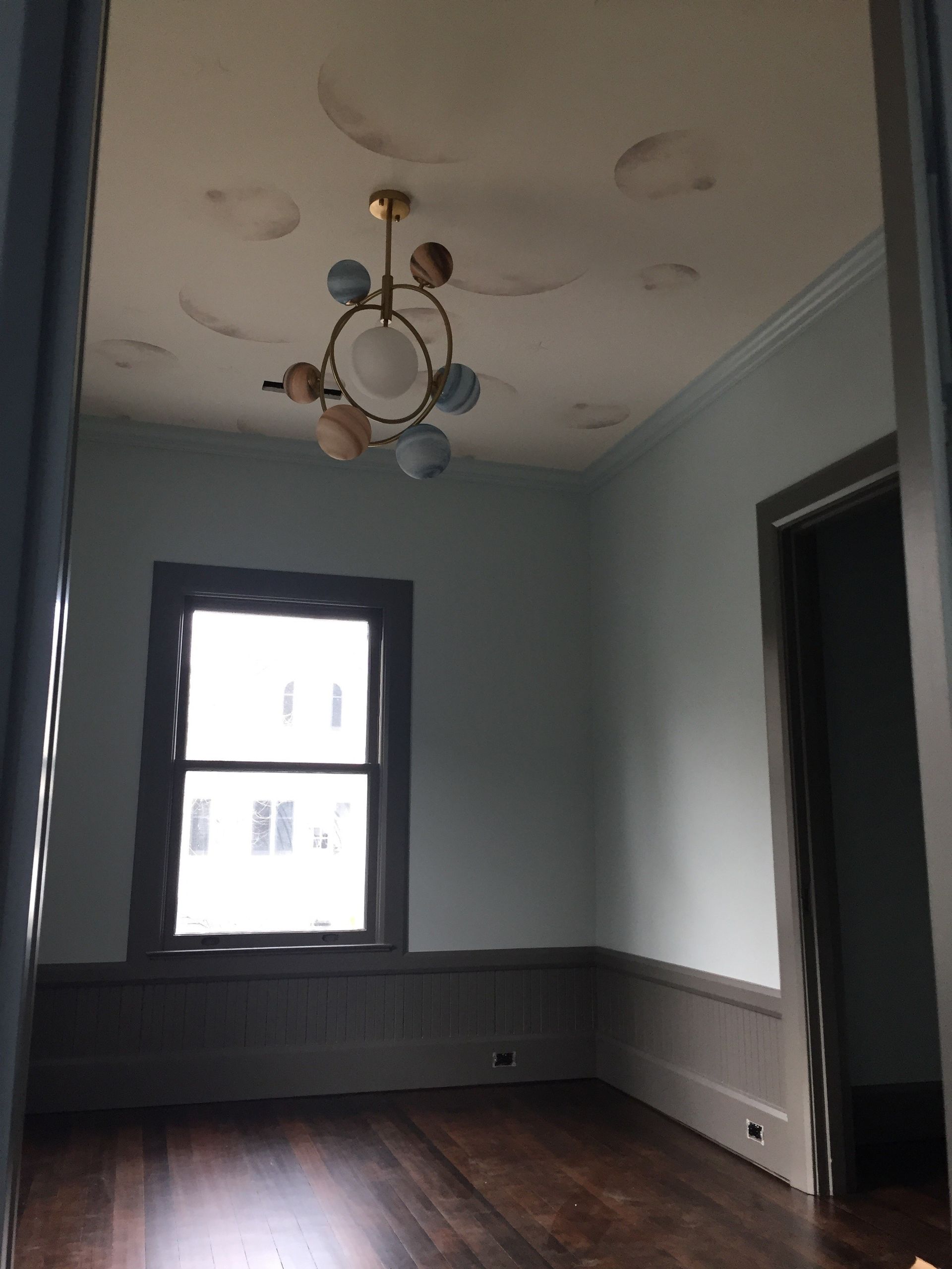 An empty room with a window and a chandelier hanging from the ceiling