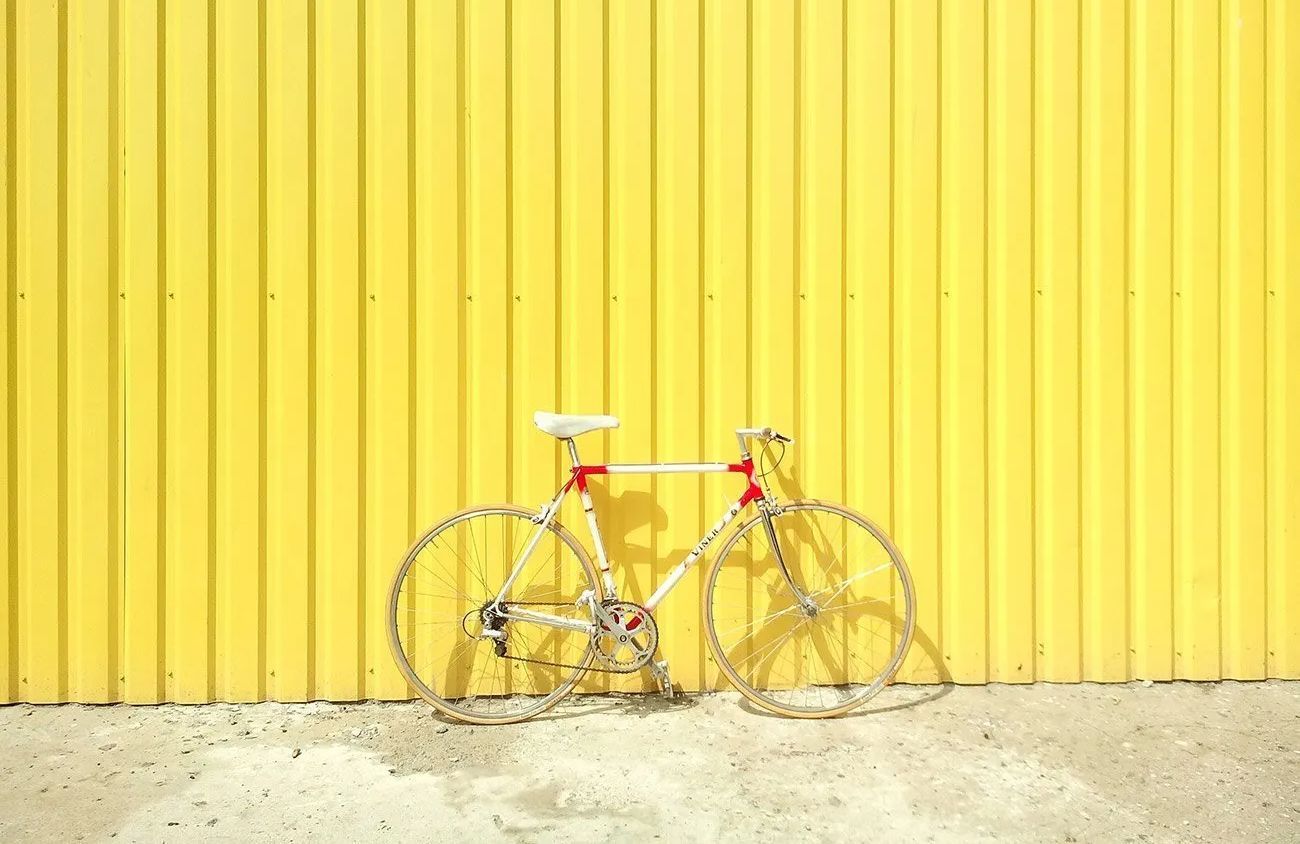 A white bicycle is leaning against a yellow wall.