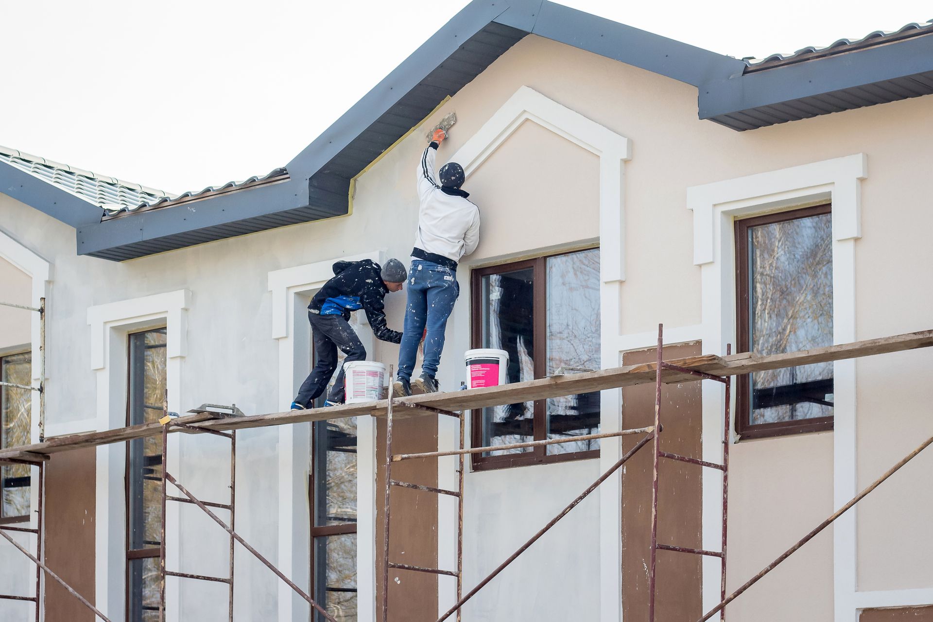 Two men are painting the side of a building on scaffolding.