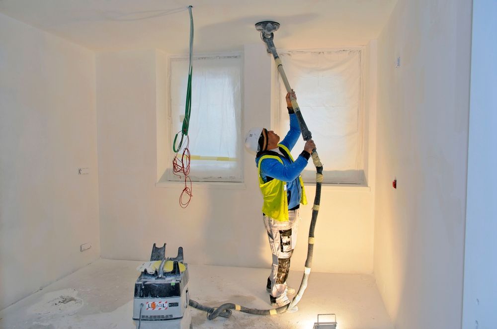 A man is painting the ceiling of a room with a vacuum cleaner.