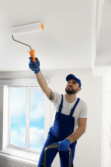 A man is painting the ceiling with a paint roller.
