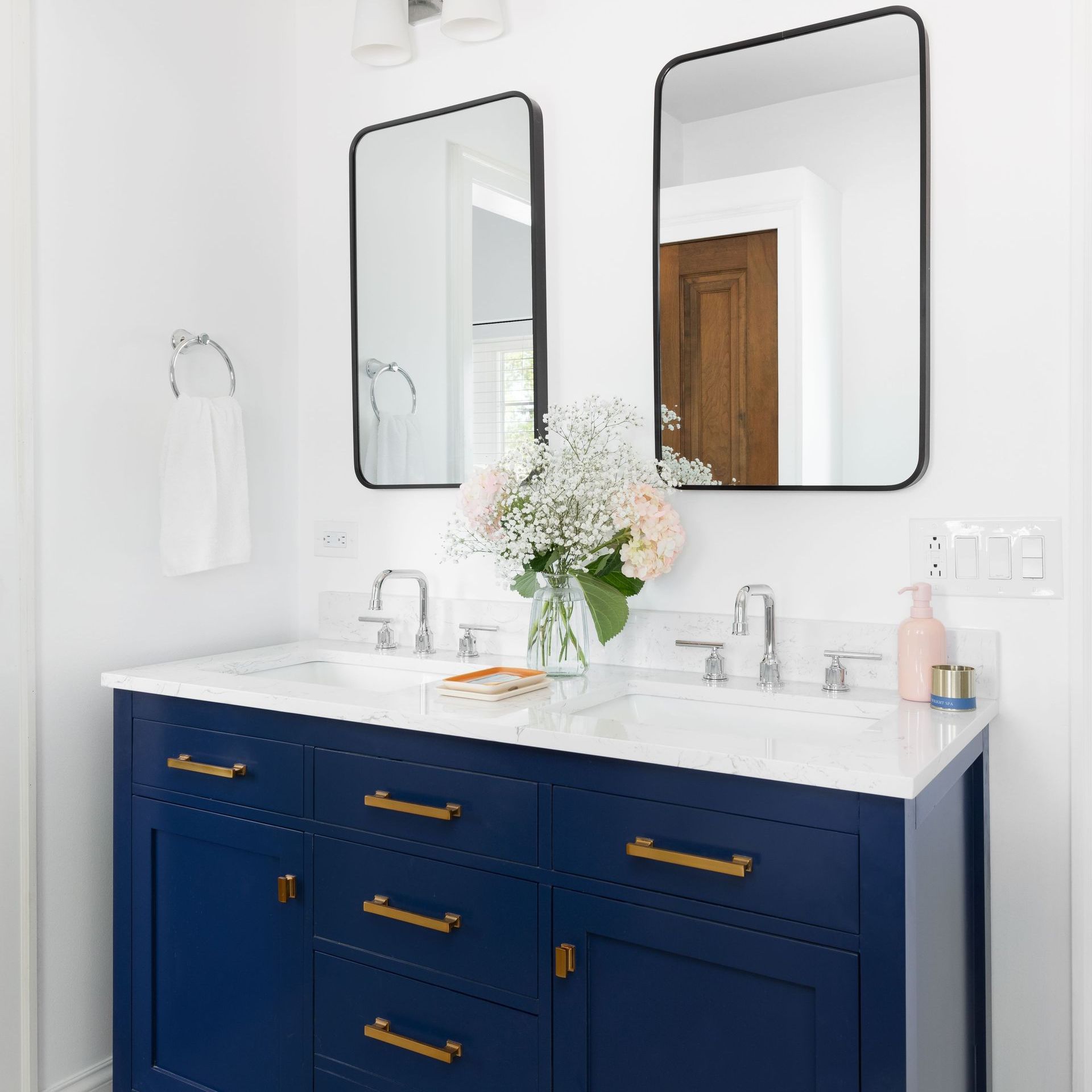 A bathroom with a blue vanity and two mirrors.