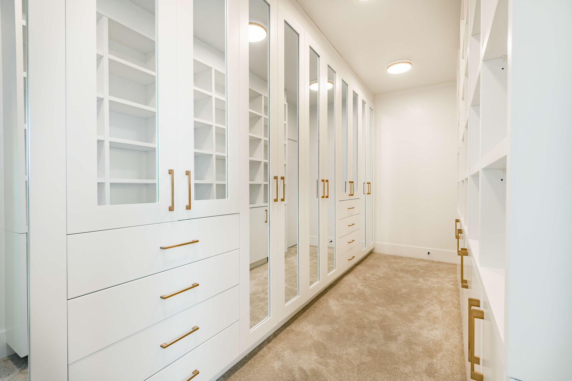 A walk in closet with white cabinets , drawers , and mirrors.