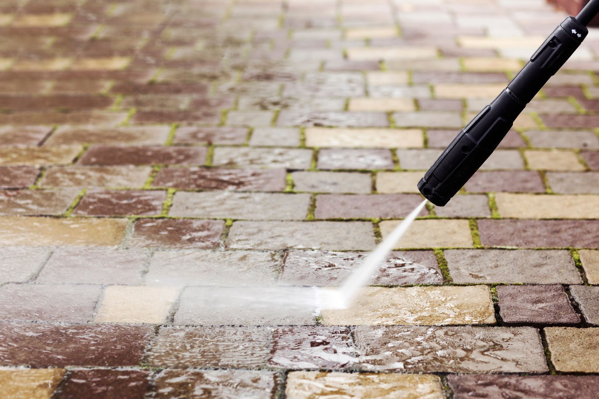 A person is using a high pressure washer to clean a brick walkway.