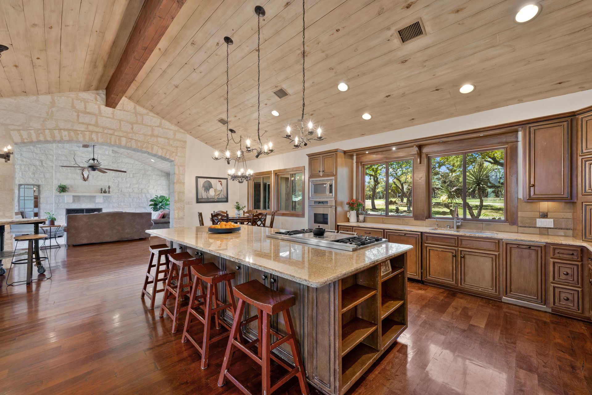 Spacious kitchen with island seating, wood cabinets, and a view to the outside. It has a vaulted wood beam ceiling and wooden floor.