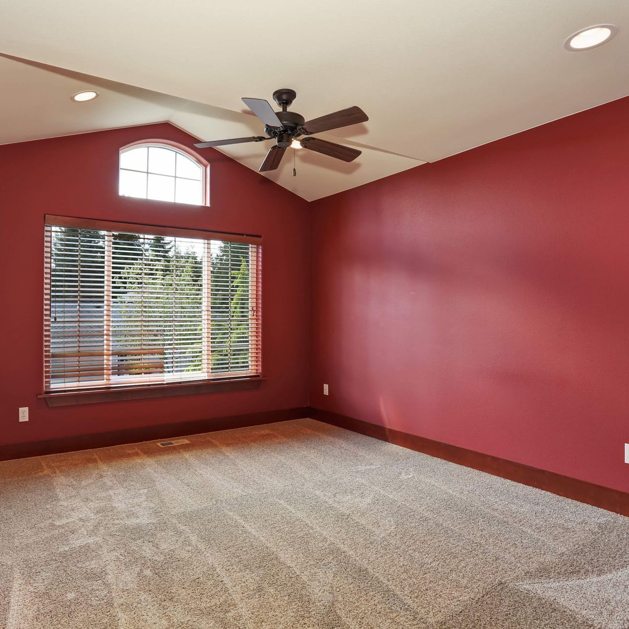An empty bedroom with red walls and a ceiling fan.