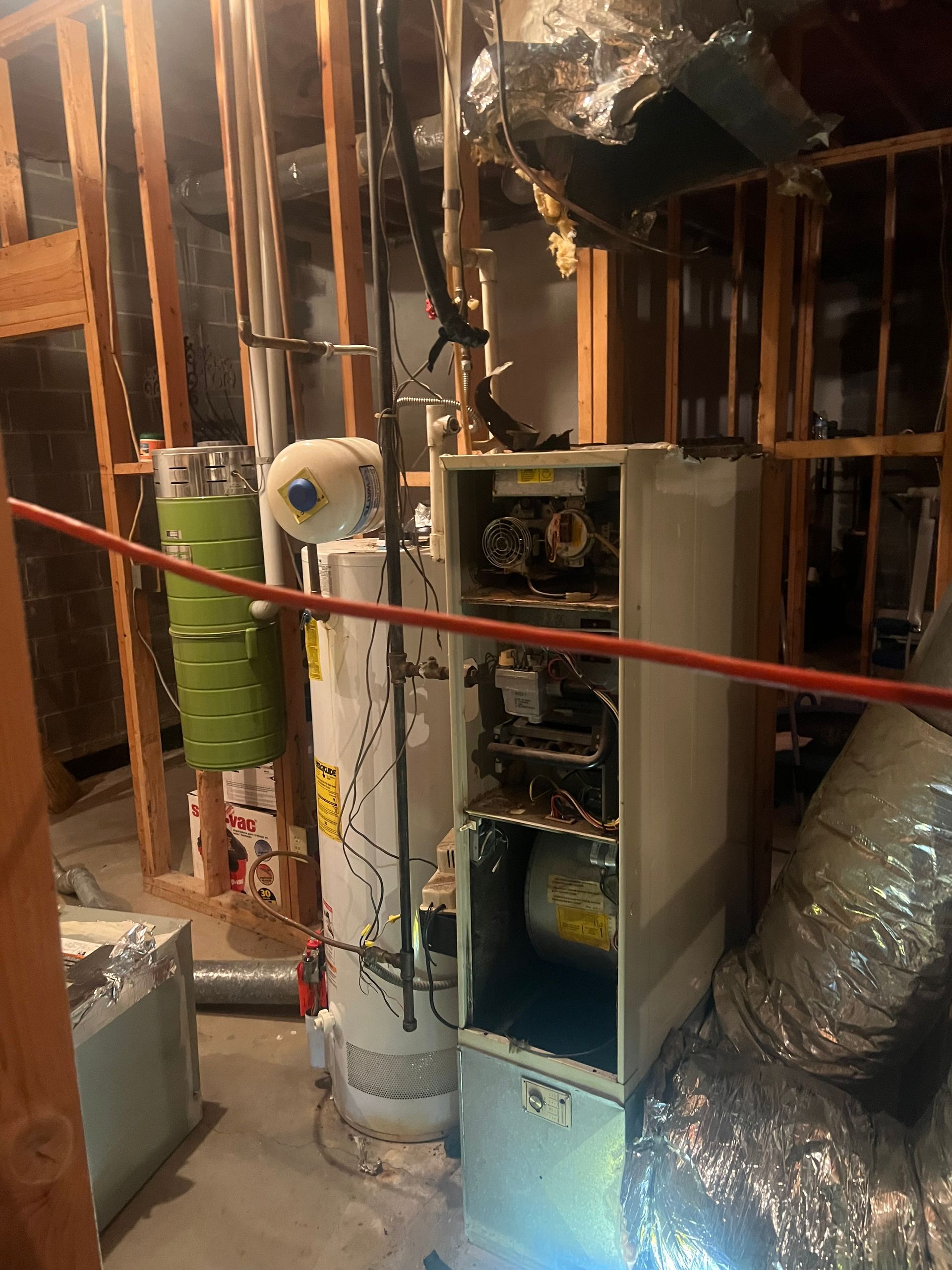 Furnace and water heater in a basement with exposed wood framing and ductwork.
