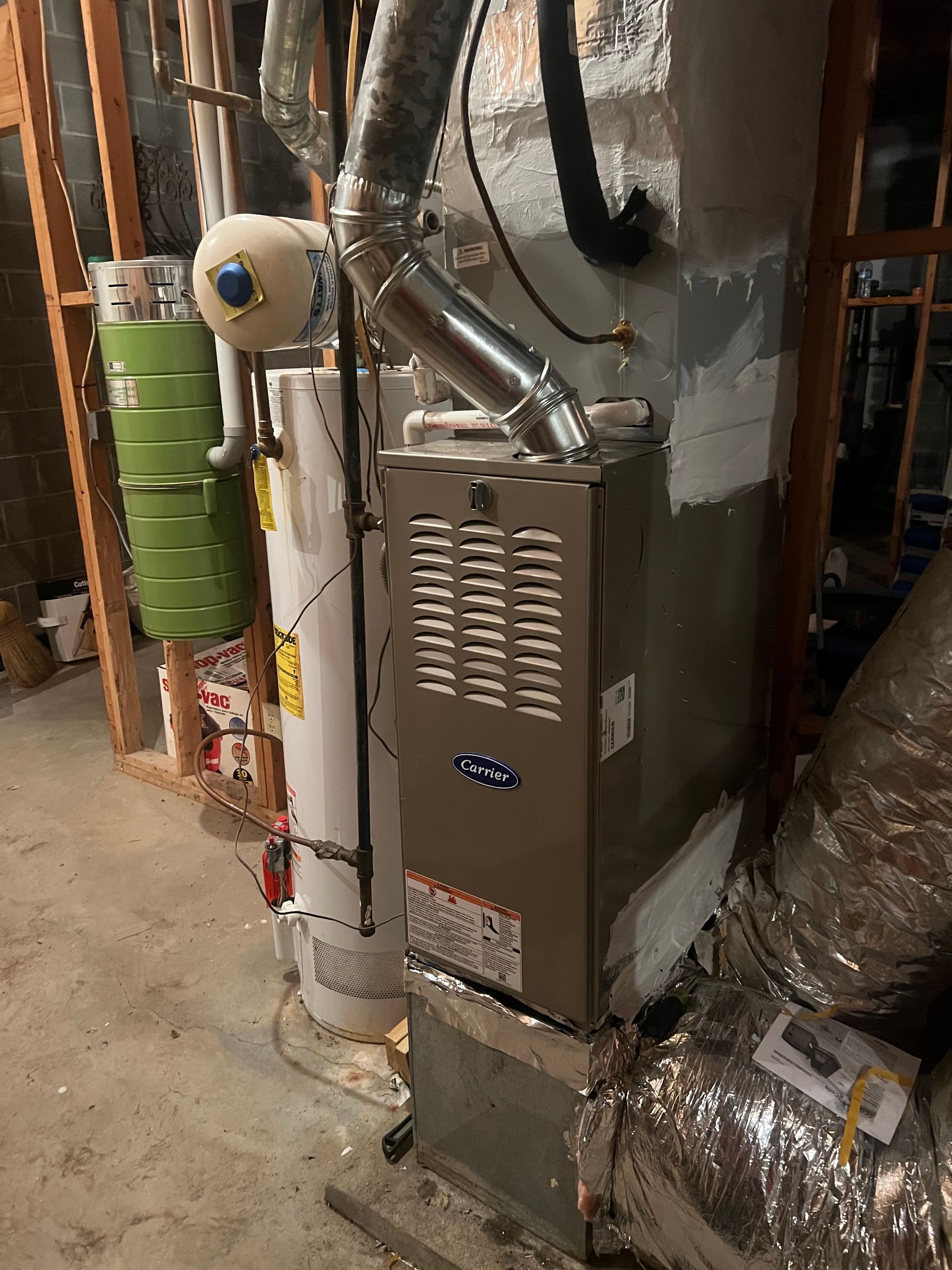 Furnace and water heater in a basement. Silver furnace, white water heater, exposed wood studs.