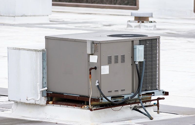 Rooftop air conditioning unit with gray metal housing, surrounded by white roofing and conduit.