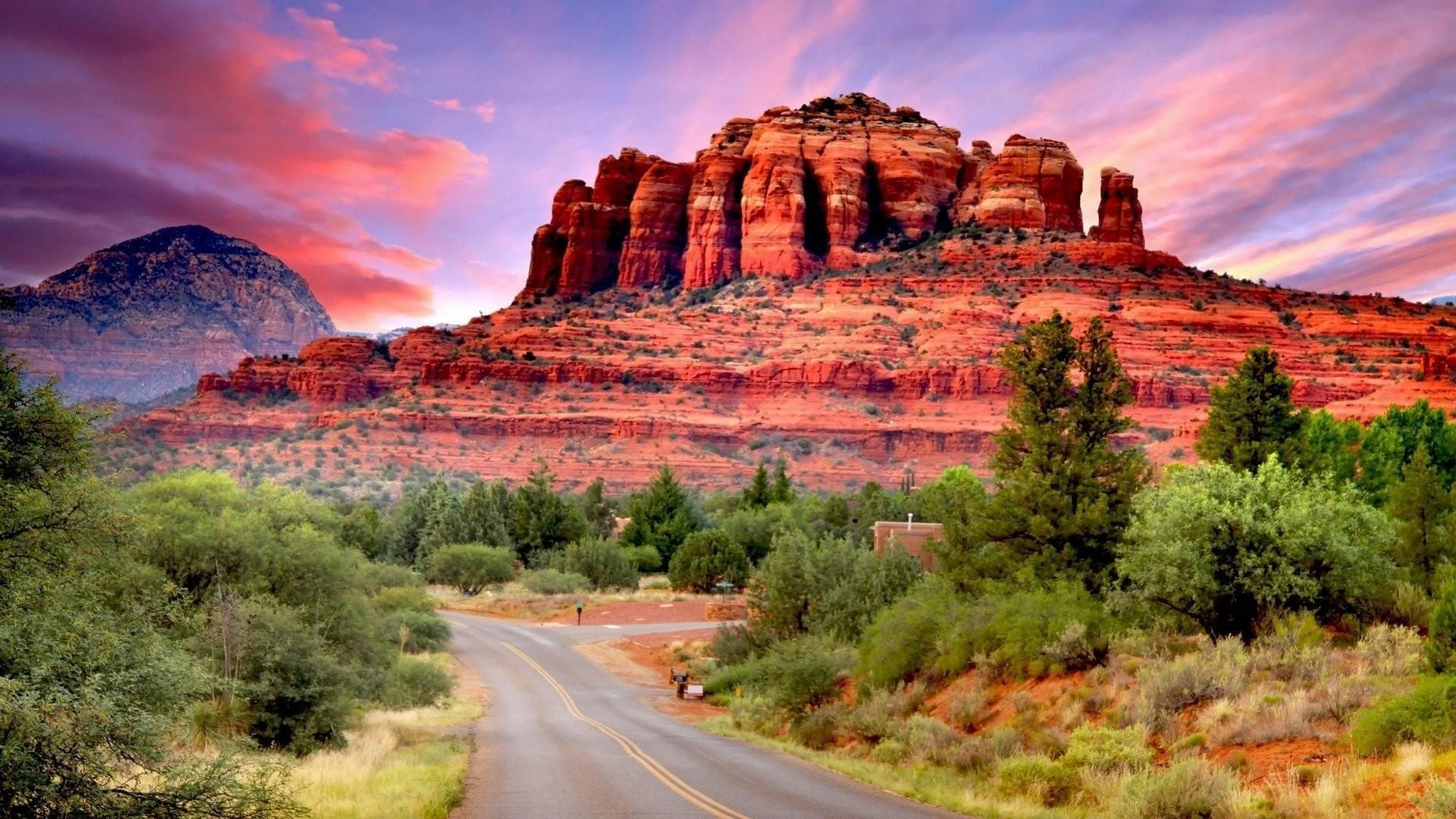 Road leading to a red rock formation under a pink and orange sunset in Sedona, Arizona.