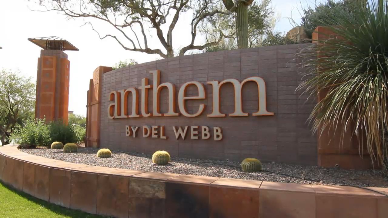 Sign for Anthem by Del Webb, brown with gold lettering, in a desert landscape.
