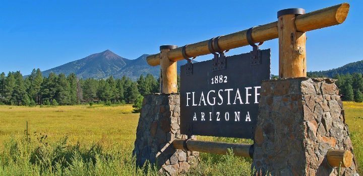 Flagstaff, Arizona, welcome sign against a backdrop of a mountain, blue sky, and green and yellow fields.