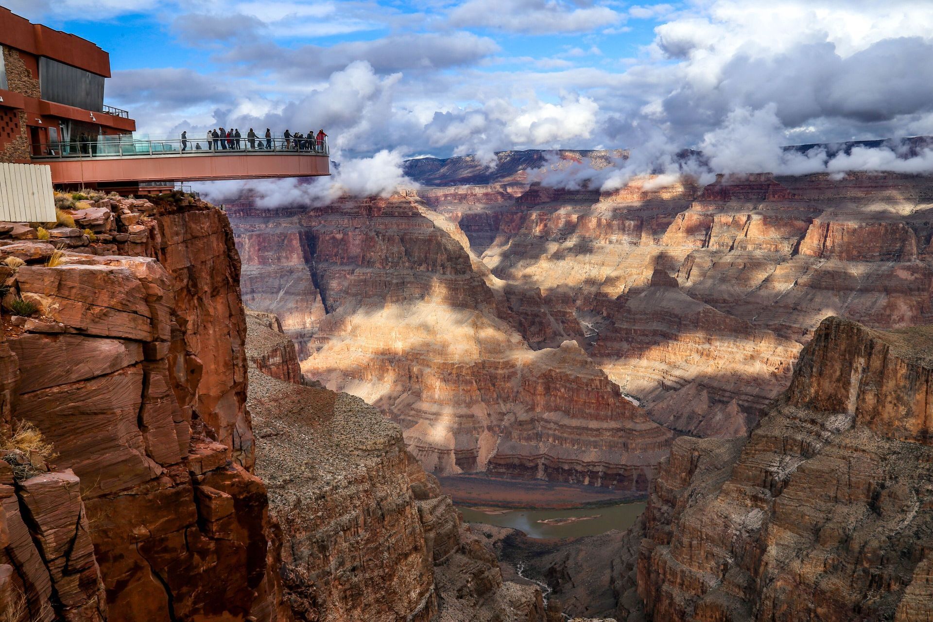 Grand Canyon Skywalk with visitors, overlooking the canyon under a cloudy sky.