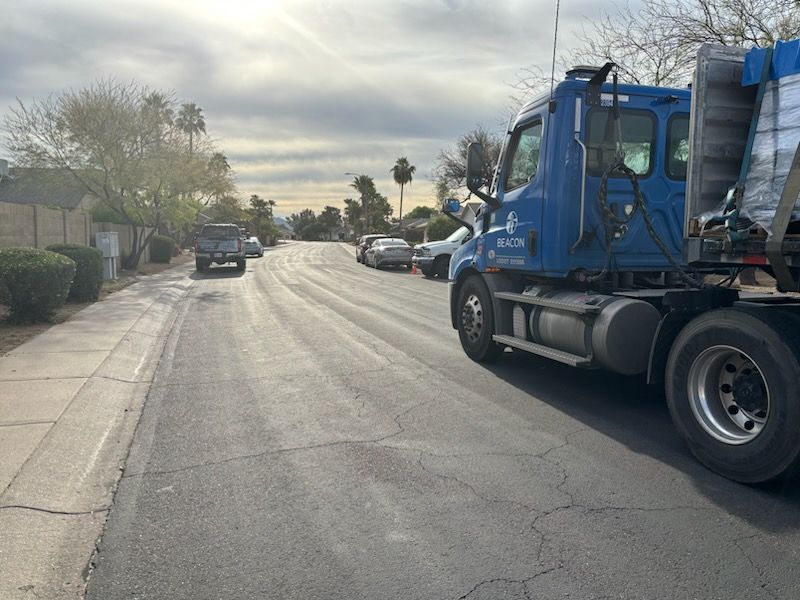 Blue semi-truck on residential street with cars. Overcast sky.