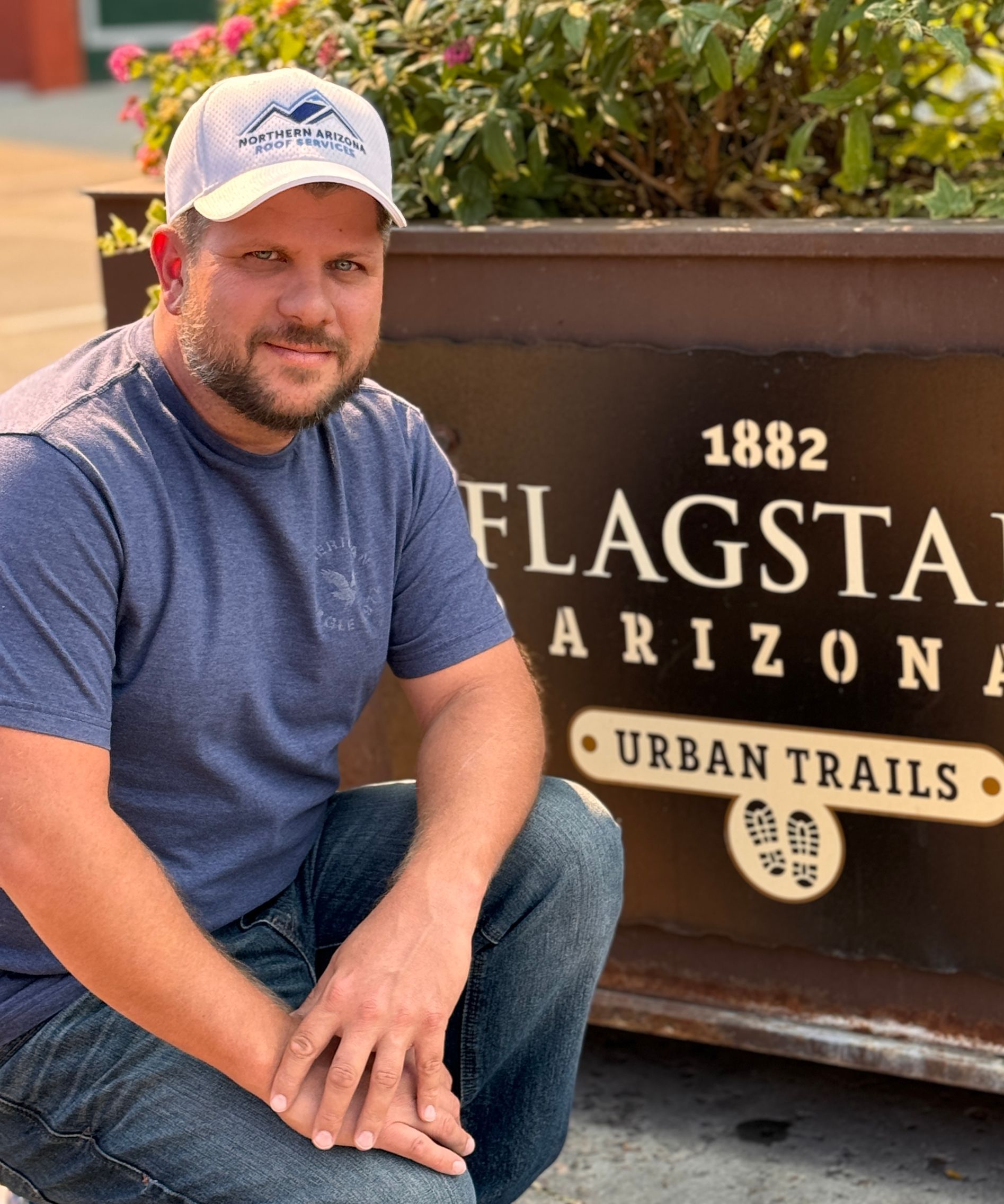 Man in blue shirt and jeans kneels near a planter that says